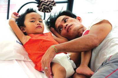 8月13日，在菲律宾一处登革热应急医疗站，一名父亲照顾自己患病的孩子。新华社照片