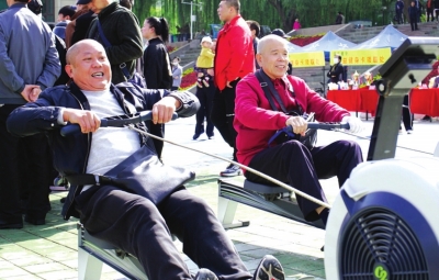 ③两位市民在赛场外的划船机上体验运动的快乐。